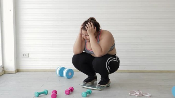 胖女人在健身室称重体重秤后做压力大的手势。加大码胖成熟女人或概念