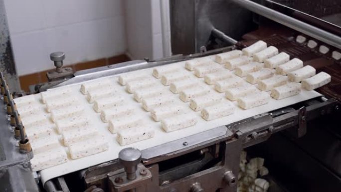 糖果厂的生产线上的糖果与巧克力一起倒入。甜食生产线。干酪棒的制造工艺。食品工厂
