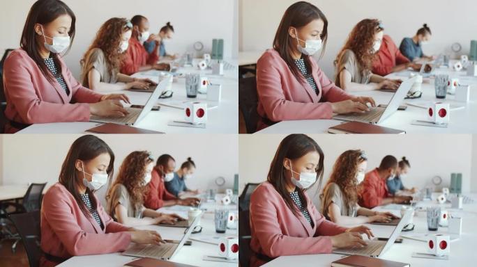 工作日在办公桌上戴口罩的女人使用笔记本电脑