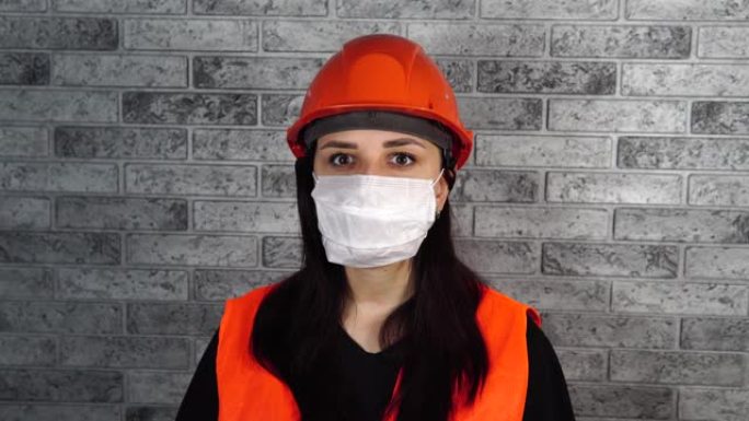 灰色砖墙背景下脸上戴着医用面具的年轻女子肖像。成年女性用口罩遮住脸，以保护自己免受疾病的侵害。冠状病