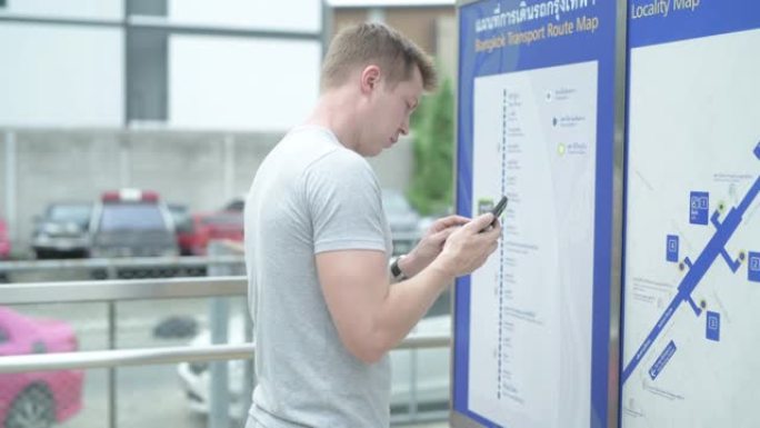 年轻的游客在曼谷火车站检查地图并使用电话指示
