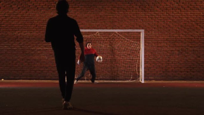 两个年轻朋友晚上在户外操场踢足球-保护大门
