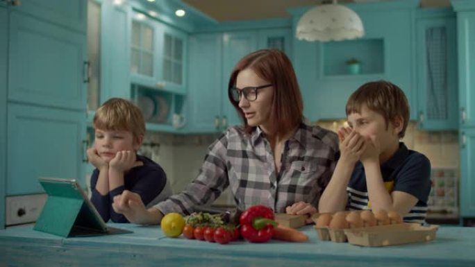 一家人一起烹饪站在蓝色厨房的平板电脑上看在线食谱。两个孩子在家帮妈妈做饭。