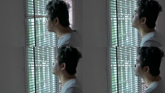 亚洲男子醒来，透过卧室的窗户看，生活中的概念日发热新型冠状病毒肺炎检疫