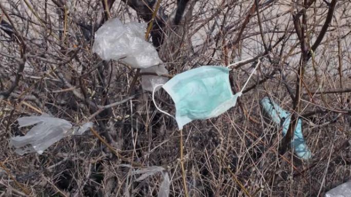 树枝上的口罩和塑料碎片。冠状病毒 (新型冠状病毒肺炎) 正在造成污染，因为废弃的口罩和塑料垃圾一起使