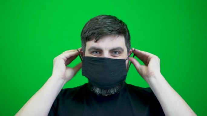 在冠状病毒大流行期间，一个大胡子的人戴上了许多医用口罩。绿色背景上一张脸的特写。