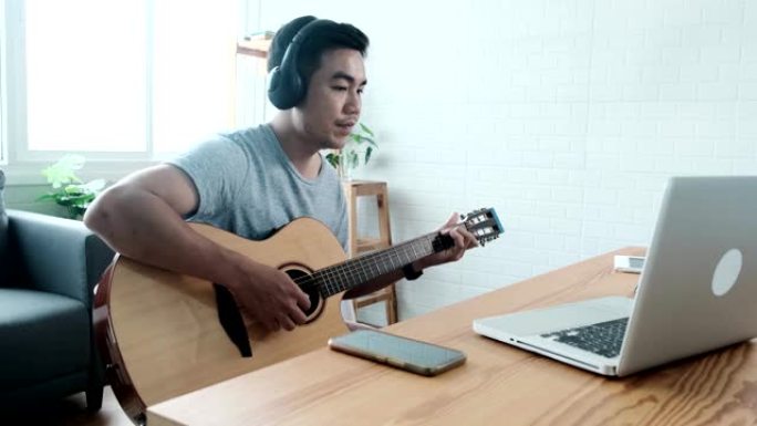 亚洲男子在家用笔记本电脑学习和练习在互联网上弹吉他