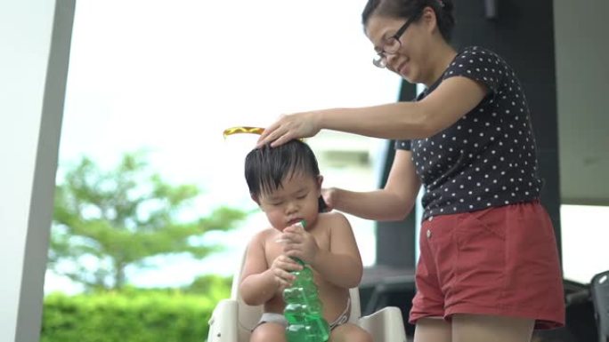 亚洲母亲在露台上剪下了蹒跚学步的儿子的头发。