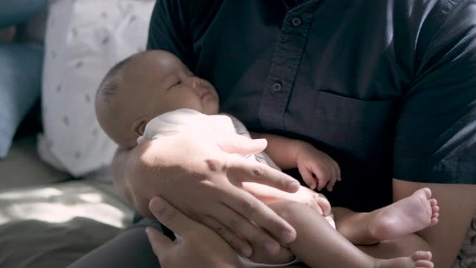 一位亚洲父亲将一个熟睡的婴儿抱在膝盖上