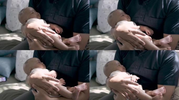 一位亚洲父亲将一个熟睡的婴儿抱在膝盖上