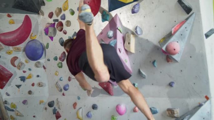 年轻的大胡子肌肉发达的运动员在攀岩墙上跳跃
