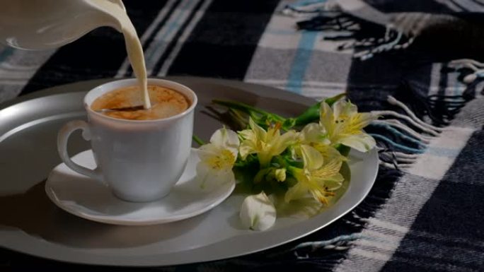 将送牛奶的牛奶倒入白杯和热咖啡中。早上早餐概念。床上早餐。在卧室托盘上的一杯温暖的卡布奇诺咖啡中添加