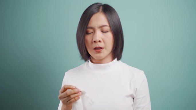 亚洲妇女因发热打喷嚏而生病，并被隔离在蓝色背景上的薄纸擦拭鼻涕。医疗保健概念。4k视频。