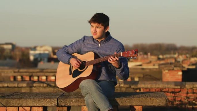 夕阳下的年轻人在房子的屋顶上弹吉他。自由概念