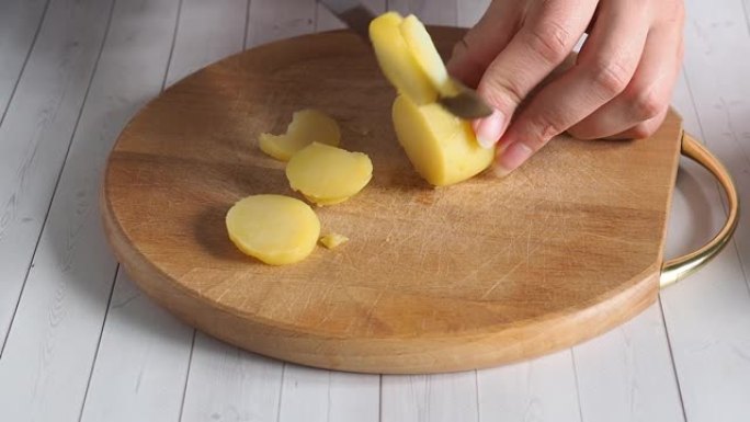 库克将煮熟的土豆切成幻灯片。在木制砧板上切土豆。