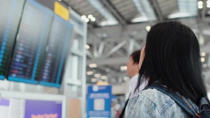 亚洲旅行者妇女在机场的计时板上检查飞机的飞行