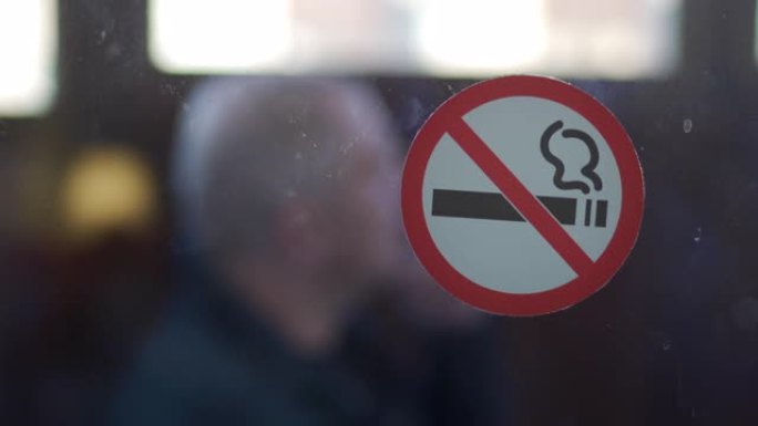 玻璃门上禁止吸烟标志，阳台上吸烟的人。