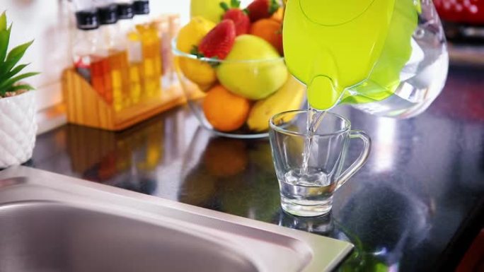 将过滤后的水从厨房的水罐倒入玻璃杯中