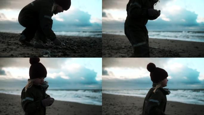 穿着冬装的女孩在海滩上捡鹅卵石