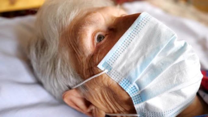 戴着病毒防护面具的老妇人的特写脸。生病的女士带着悲伤的视力和医用口罩躺在医院的床上。健康或安全生命的