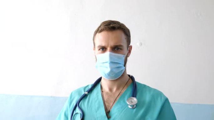 戴着医用口罩的年轻男性白人医生的肖像看着相机。医务人员戴着病毒的防护口罩。冠状病毒大流行带来的健康和