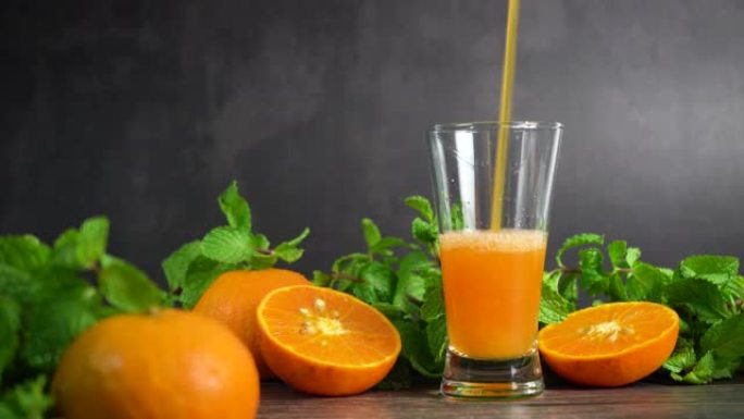 将新鲜的橙汁倒入带有橙子水果和薄荷的玻璃杯中，放在桌子上，健康食品中。