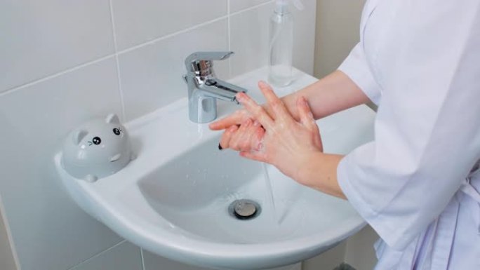 关闭女性医学专家在医院洗手和消毒。女人用肥皂泡沫彻底洗手，然后在自来水下冲洗。侧视图