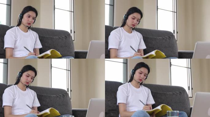亚洲快乐的年轻女子学生戴着耳机在线学习在笔记本电脑上观看网络研讨会播客听力学习教育课程会议打电话和写