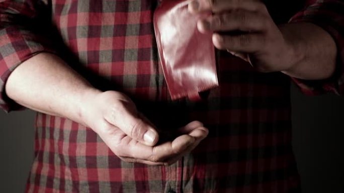 穿着红色衬衫的男人从棕色皮革钱包里倒格里夫纳硬币到他手里，贫穷概念到他手里