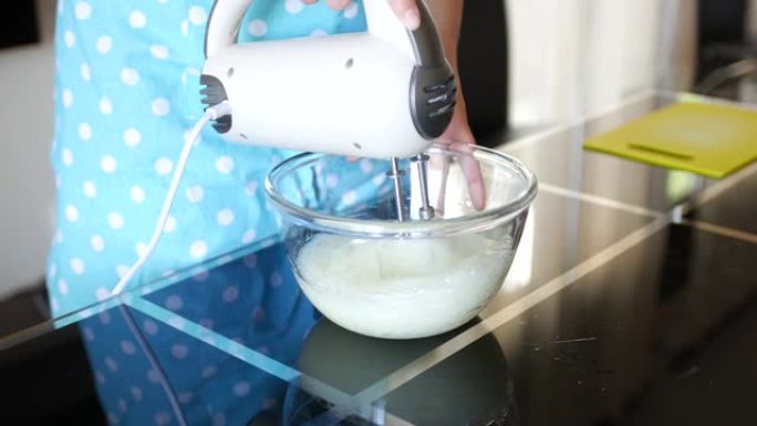 女厨师将蛋清与玻璃透明碗中的搅拌器混合成白色通风泡沫状态。