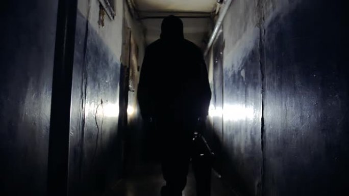 穿着黑色夹克，背着包的匪徒沿着走廊离开摄像头