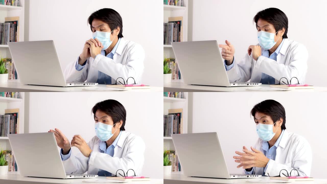 亚洲男性医生戴着口罩，通过视频会议系统与笔记本电脑一起工作