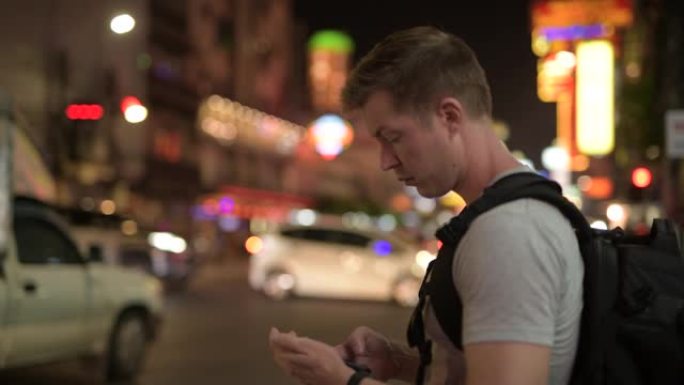 年轻的游客背包客在晚上在唐人街打电话和叫出租车时等待