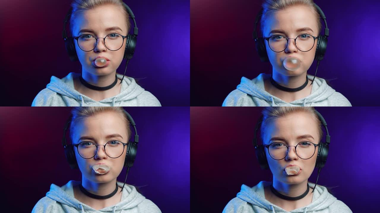 时髦女孩的肖像吹泡泡糖隔离在迪斯科霓虹灯。在4k红色相机上近距离拍摄