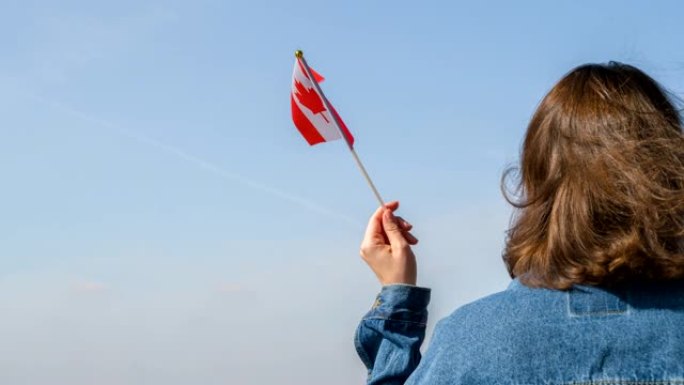 一个孤独的女孩，穿着牛仔夹克，在蓝天的背景下举着不同国家的国旗。和平、友谊、统一。