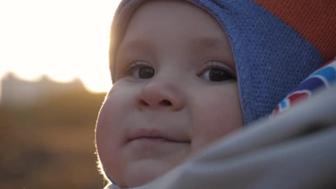可爱的微笑小婴儿在夕阳下散步时穿着暖和的衣服的肖像