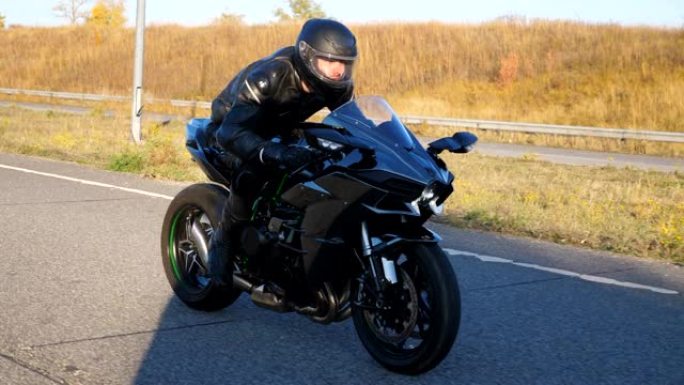 秋季，戴着头盔的男子在高速公路上骑摩托车的侧视图。摩托车手在日落时在乡间小路上驾驶摩托车。自由和冒险