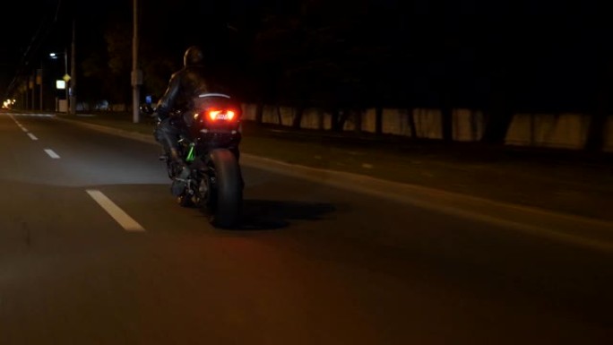 摩托车手在夜城赛车。在小镇的夜间街道上骑着现代运动摩托车的人。旅途中开车的人。自由和冒险的概念。后视