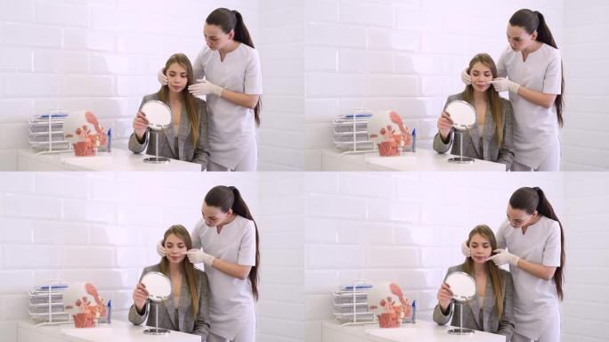 美容诊所的咨询。女美容医生与患者交谈，并用镜子显示年轻女孩的脸部变化。规划美容治疗