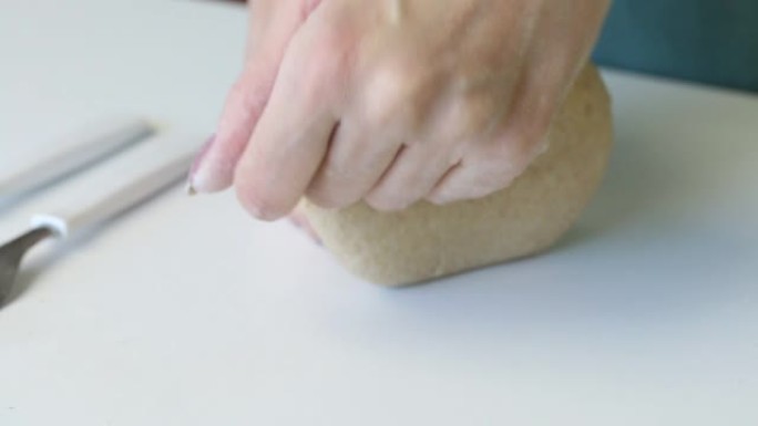 一个女人用手揉捏一块生面团做新鲜蛋糕。桌子表面附近有rolling面杖和面粉。准备无酵饼。特写