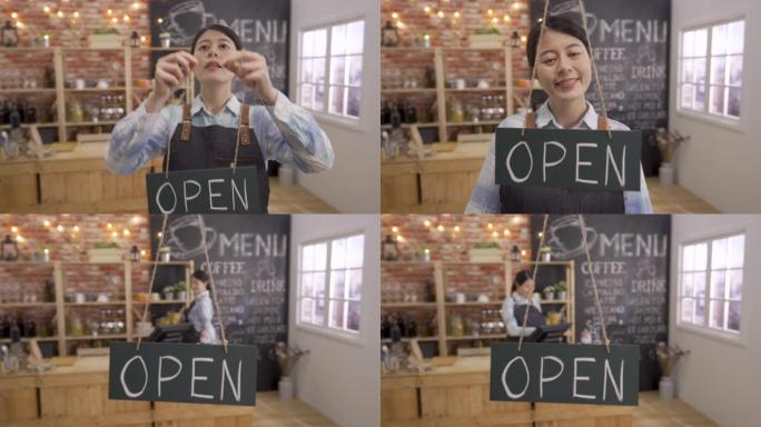 美丽的年轻亚洲女咖啡馆老板悬挂店面标志，欢迎新顾客进入现代时尚的咖啡店。女服务员走得关门，笑脸相机回
