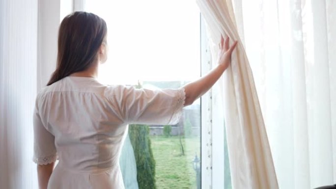 高加索年轻女子打开窗帘，透过窗户看。