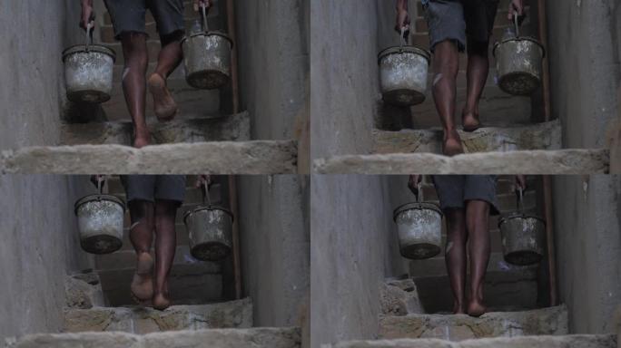 赤脚当地工人用湿水泥搬运旧水桶