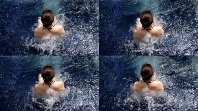 黑发女人坐在蓝色户外热水浴缸水中，白色泡沫