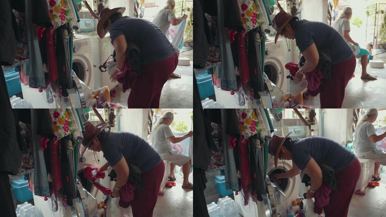 亚洲老女人把衣服从洗衣机上拿下来。在她家门前的衣服晾干。