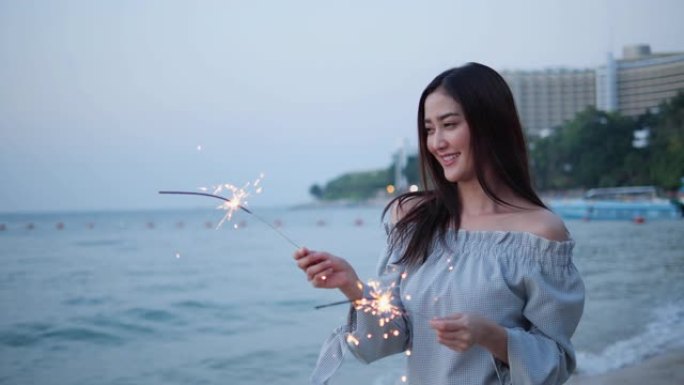 亚洲少女在海滩夏天在海边玩烟花美丽的灯光闪耀。年轻女性快乐节日和周年庆典。年轻女性是旅行博客。