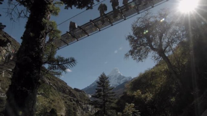 人们走在吊桥上，背景是Ama Dablam。徒步前往珠穆朗玛峰大本营。