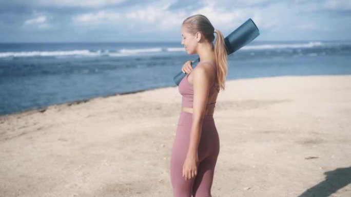 背面视图，穿着运动服和体操垫的年轻女子去海滩