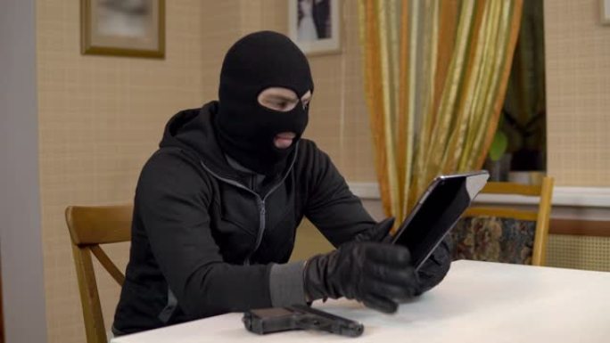 一名抢劫犯试图黑进一台平板电脑。一名蒙面暴徒坐在一所房子里，试图闯入一台平板电脑。从平板电脑窃取数据