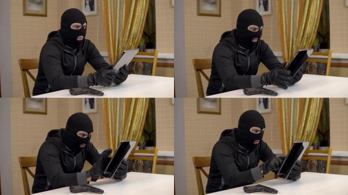 一名抢劫犯试图黑进一台平板电脑。一名蒙面暴徒坐在一所房子里，试图闯入一台平板电脑。从平板电脑窃取数据